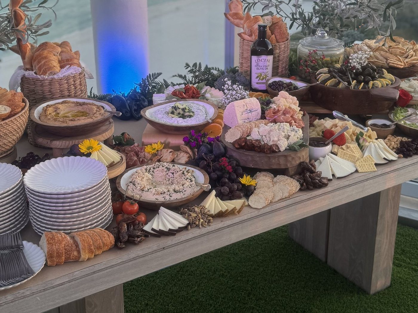 A long grazing table of dips, charcuterie, cheeses, pastries and fruit, with stacked plates at one end