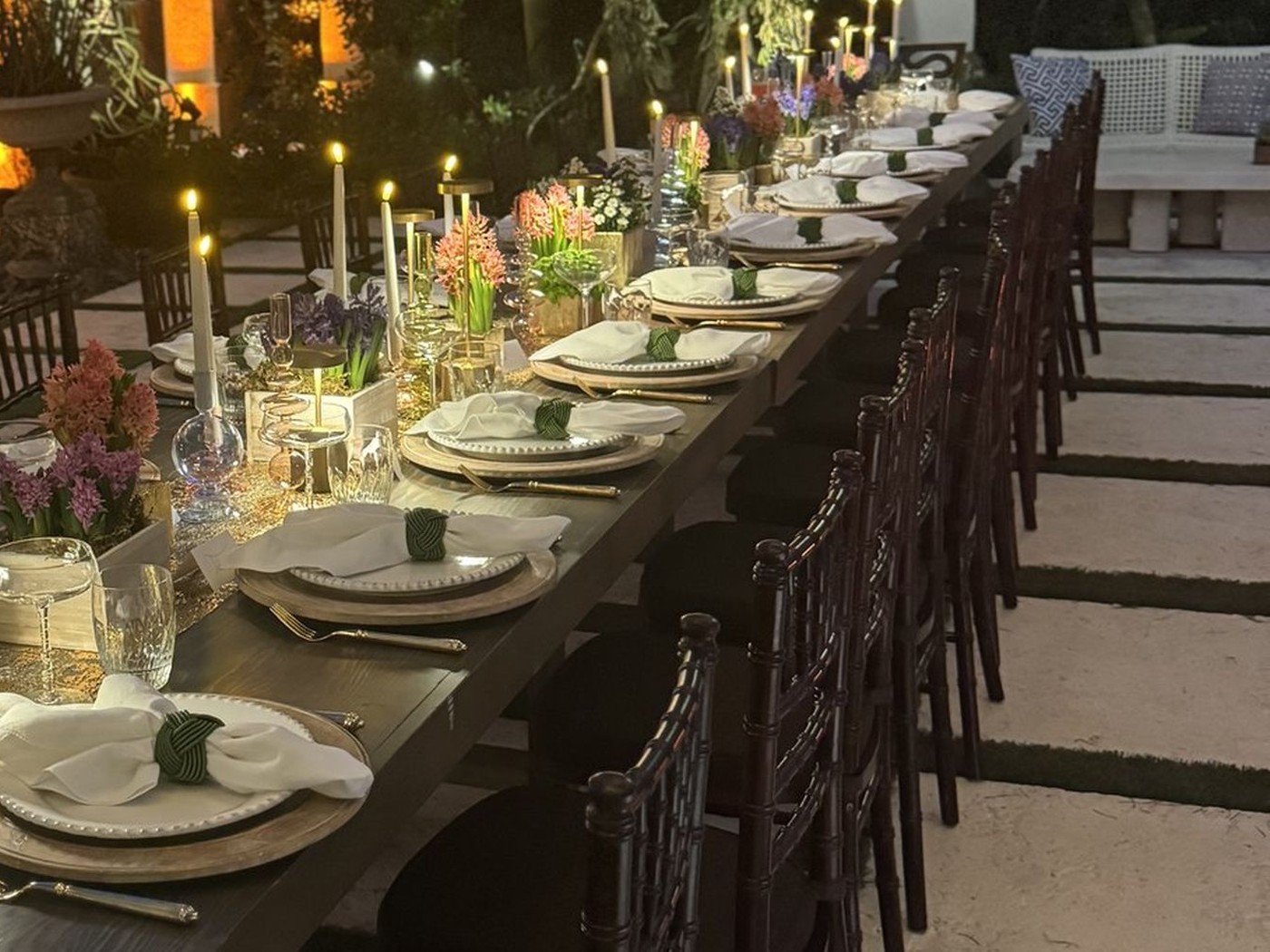 A long table laid with candles, glassware and place settings for an evening dinner outdoors in Miami