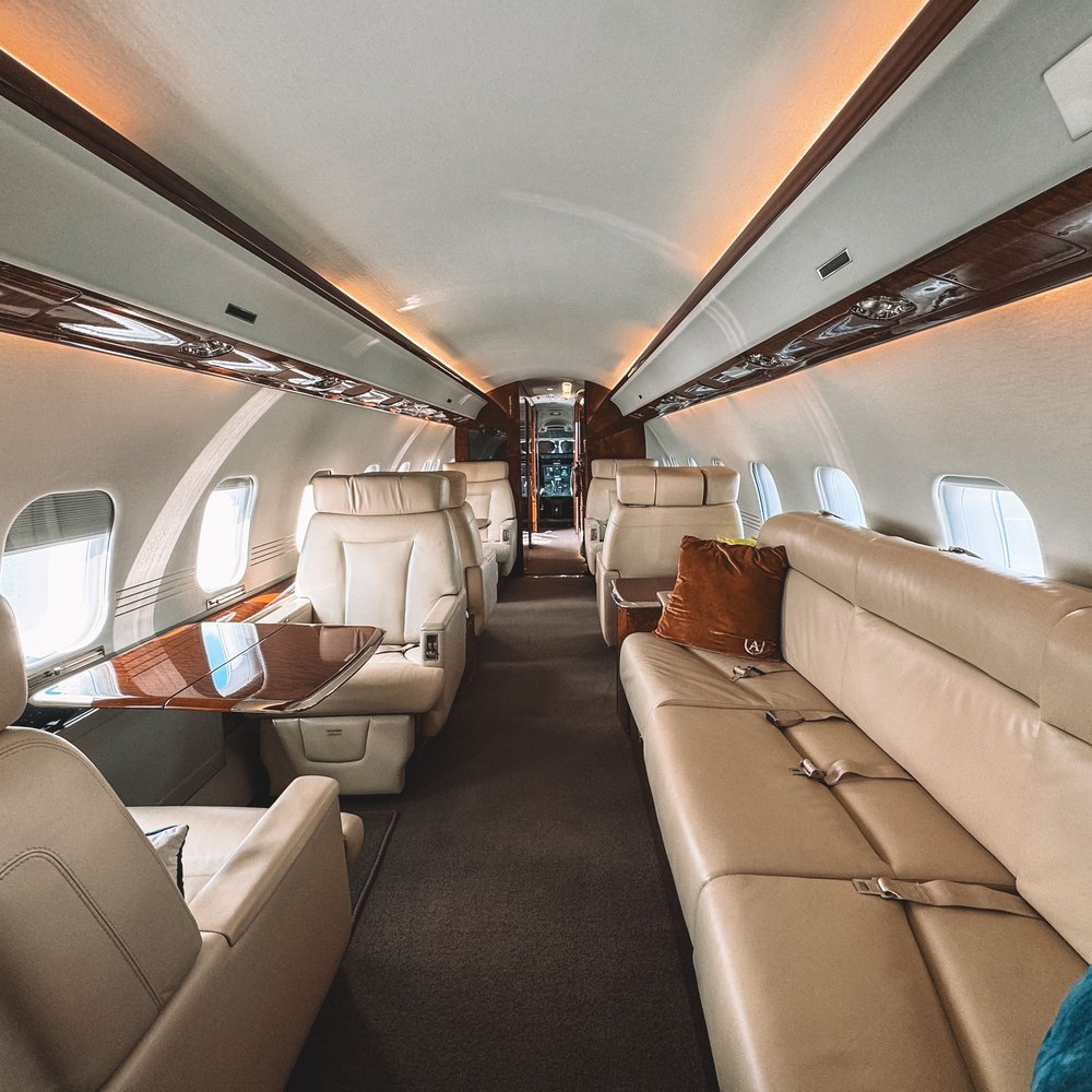 Cabin of a private jet with cream leather seating, wood trim and tables set for service