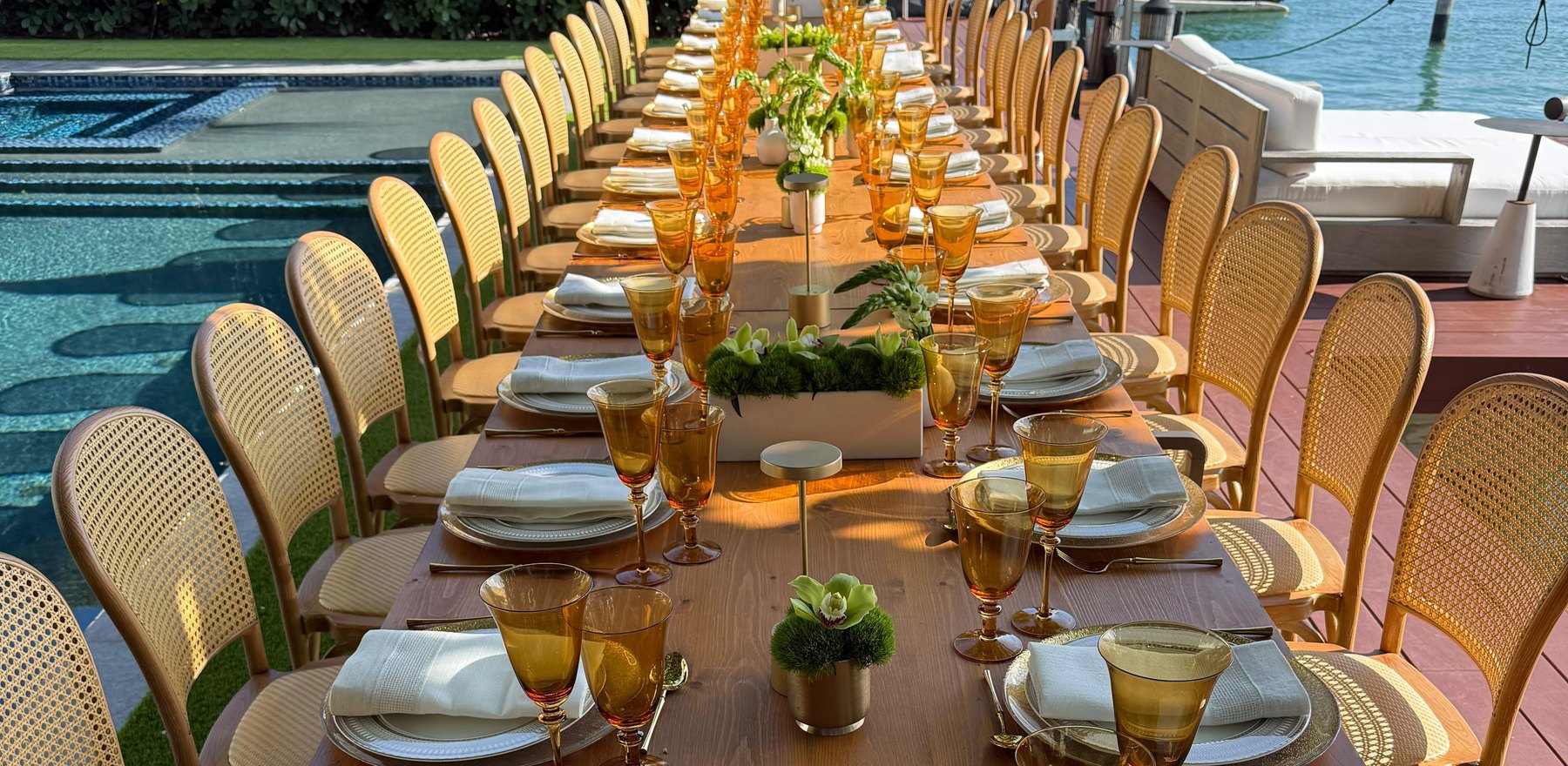 A long private dining table set beside a pool at a Miami waterfront home