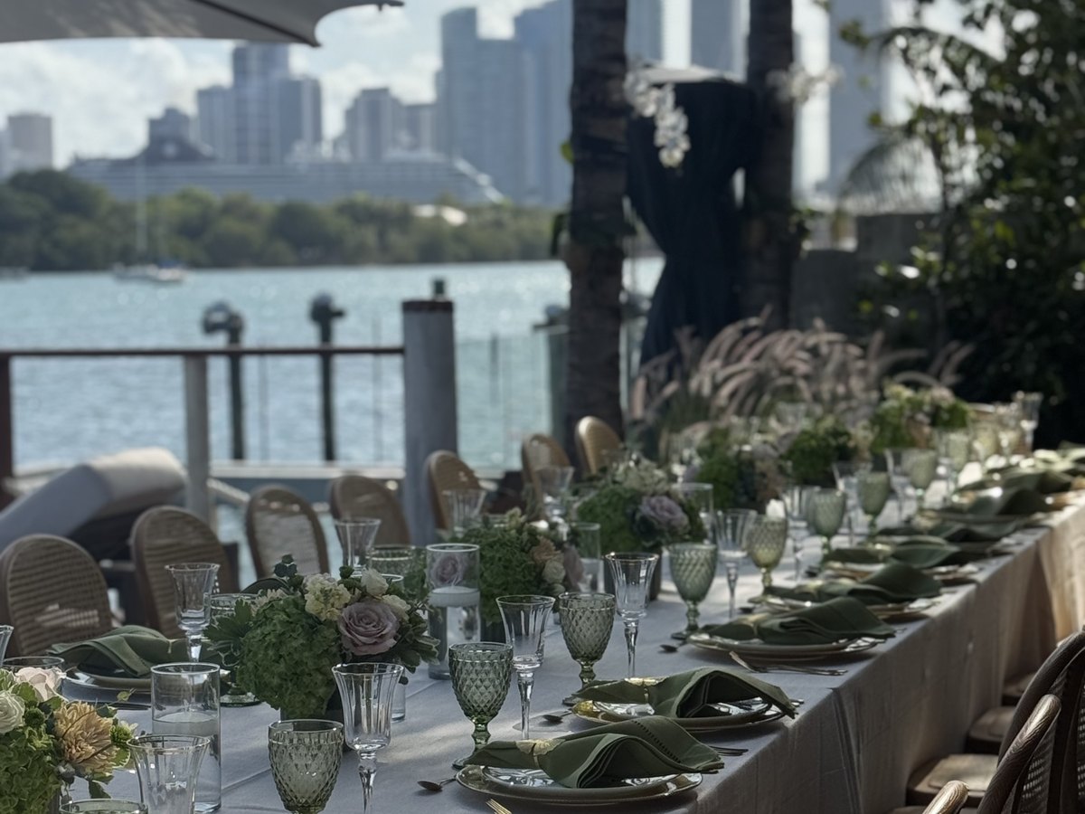 A long dinner table set on a waterfront terrace overlooking the bay and the skyline