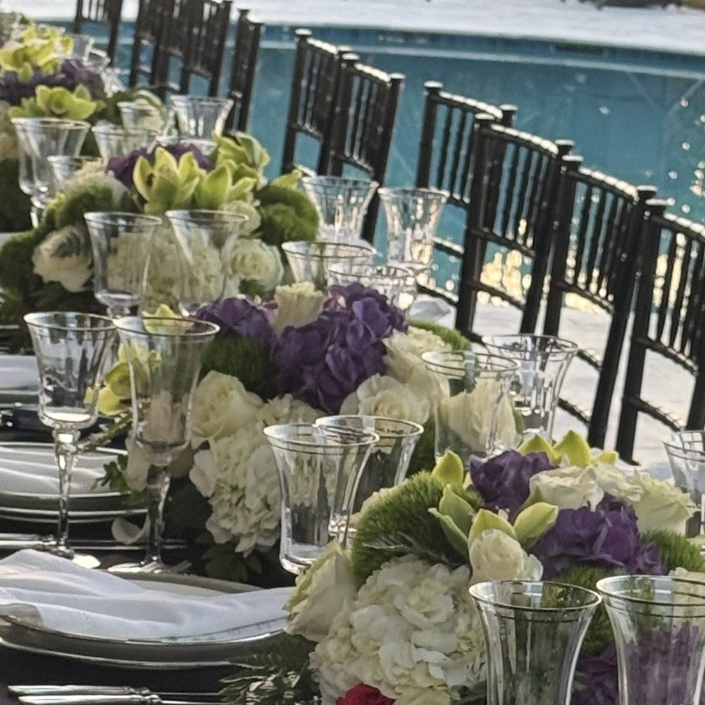A table set with white and purple hydrangeas and crystal glasses beside a pool