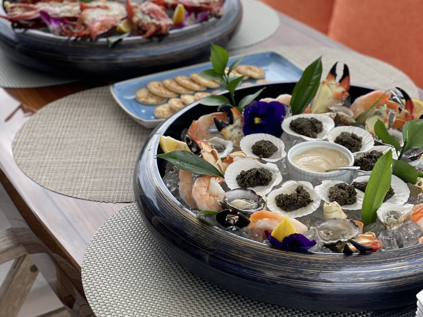 A raw bar platter of oysters with caviar, stone crab claws and shrimp on ice, set on a dressed table