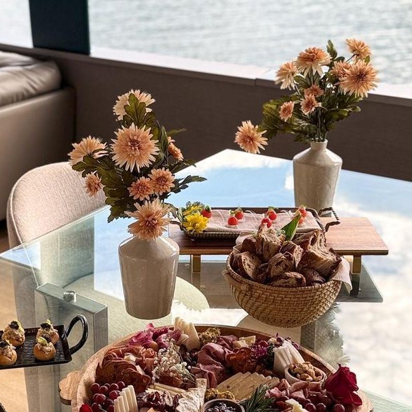 A table set aboard a yacht with a charcuterie board, pastries and canap&eacute;s, the water visible through the window behind